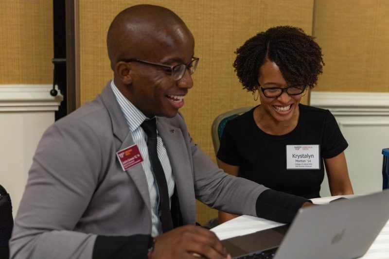 man and woman talking in front of open laptop