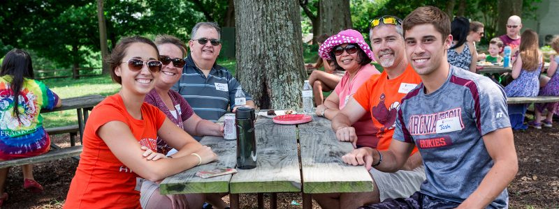 Alumni gather at a picnic table to pose for a photo during a summertime student sendoff