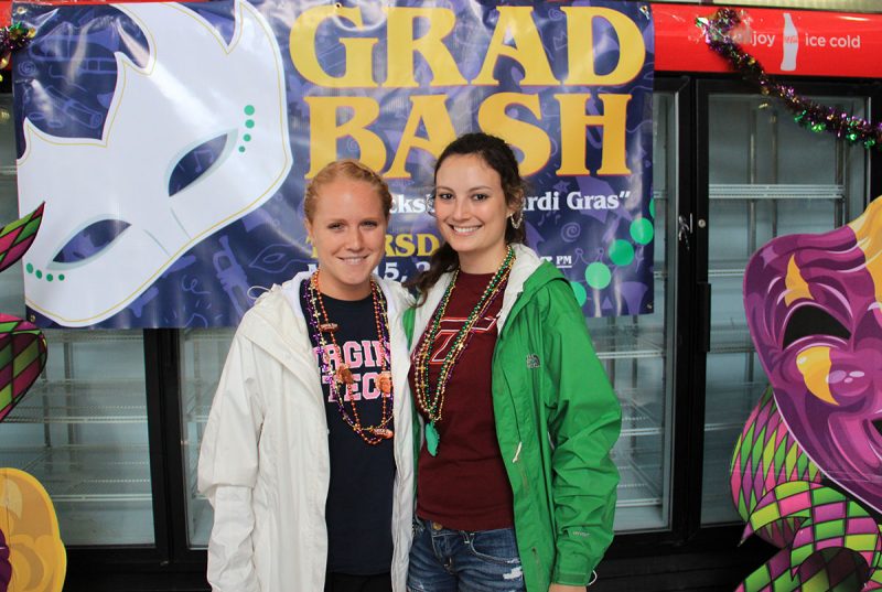Two graduates pose at Grad Bash with a giant banner for the event behind them